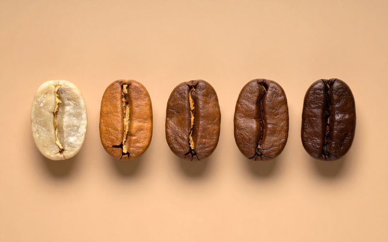 Three piles of coffee beans side-by-side, clearly showing the color progression from a light cinnamon brown to a dark, oily black.