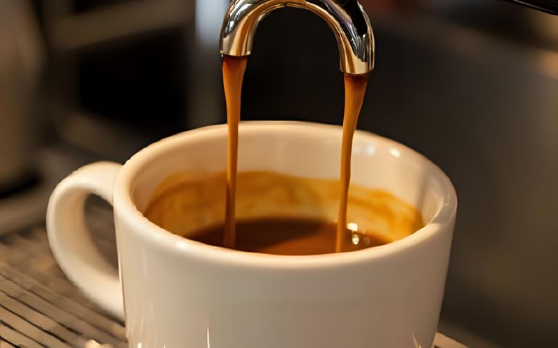 A perfect shot of espresso in a glass cup, clearly showing the distinct layers of dark liquid and the reddish-brown crema on top.