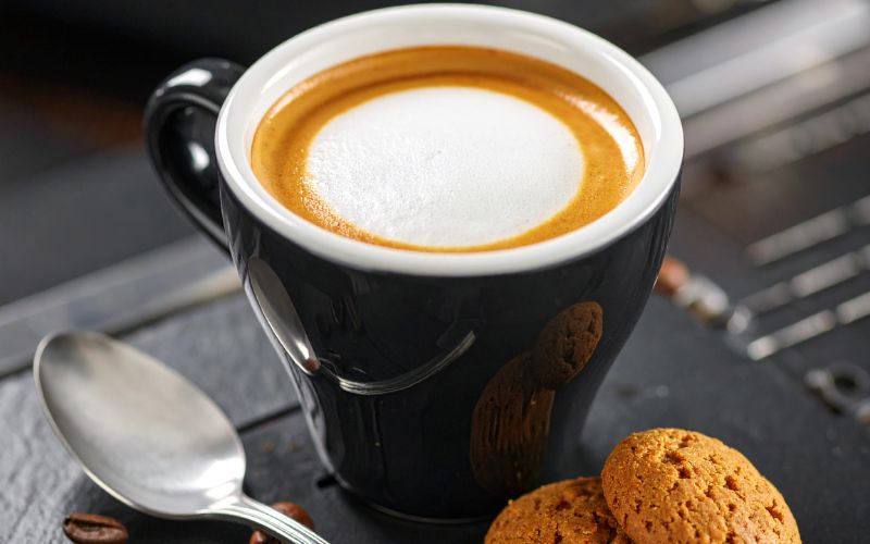 A small espresso cup with a shot of dark espresso, 'marked' with a distinct spot of white milk foam in the center of the crema.