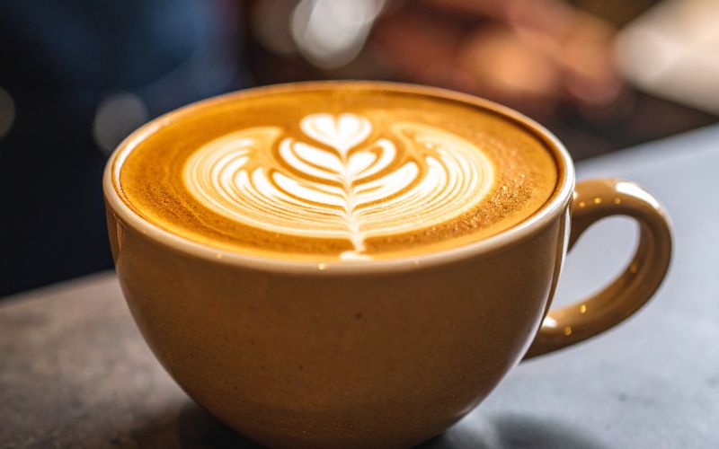 A ceramic cup filled with a freshly made Flat White, showcasing its characteristic thin layer of microfoam and a simple latte art design.