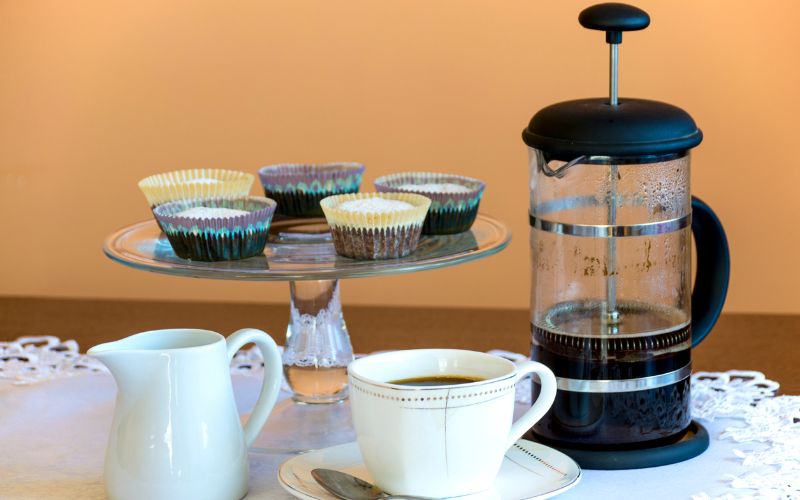 A glass French press filled with freshly brewed coffee, sitting next to a steaming mug.